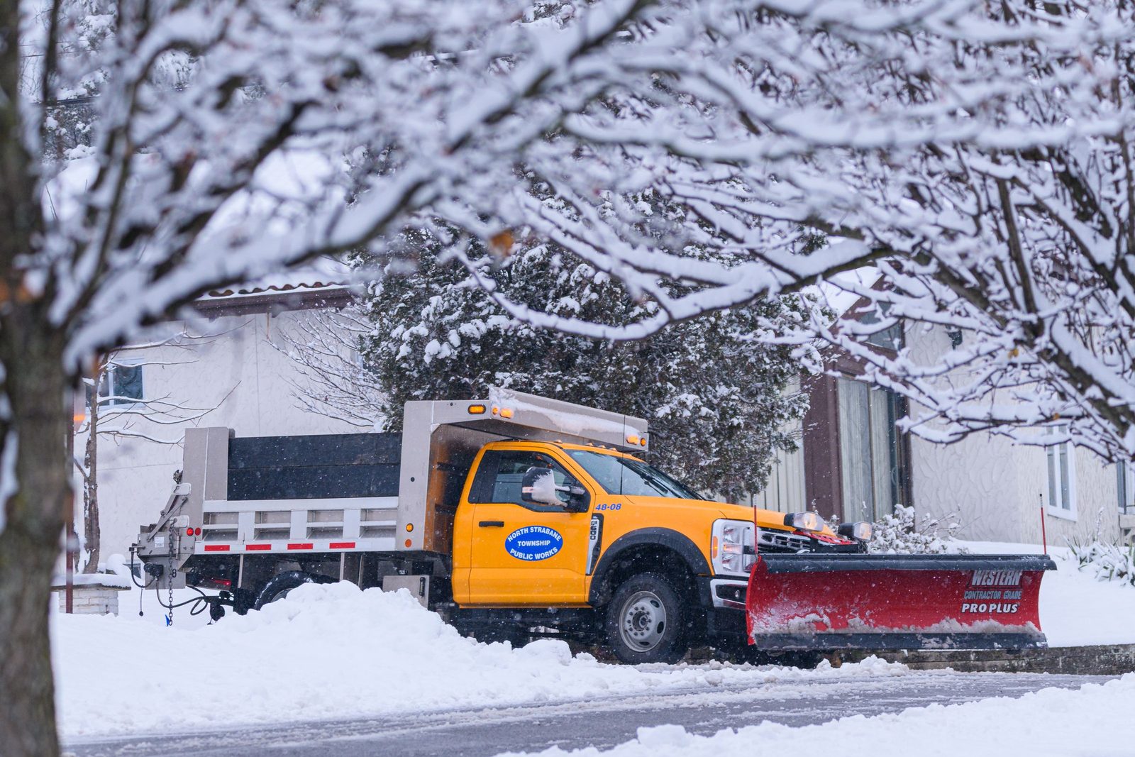 Plow truck clearing a snow-covered New England street, an example of snow removal